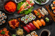 A plate of sushi with a variety of different types of sushi rolls. The sushi is arranged on a wooden board, and there are several different types of sushi, including some with avocado