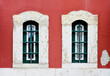 
two windows on a red wall. The windows are stylish with white frames on the wall. Exterior facade of a red historic apartment house in Lisbon, Portugal. Urban background