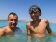 A man and young boy with goggles smiling in the sea do selfie