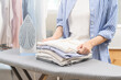 Close up young woman, girl holding stack, pile folded hygiene laundry clothes at ironing board after use electric iron steam at home. Housekeeping lifestyle, household of chores, housework concept.