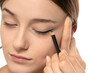 woman applying eyeliner on eyelid with pencil on a white background