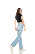 Young female model wearing ripped jeans and black shirt walking on a white background. Side, profilet view