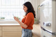 © Prostock-studio - Woman using smartphone in a sunny kitchen