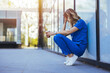 © Dragana Gordic - Tired nurse sits on floor outdoors of the medicine clinic after a hard dutty. Exhausted tired doctor or nurse. Clinic and hospital medical stuff working over hours. Overworked professional.