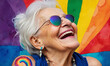 Portrait of laughing happy queer senior woman in sunglasses against a colorful rainbow background. Smiling LGBTIQA+ elderly lady celebrating Pride month. Fashionable cheerful granny with tattoo