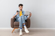 © Pixel-Shot - Handsome young man with mobile phone reading newspaper in armchair near light wall
