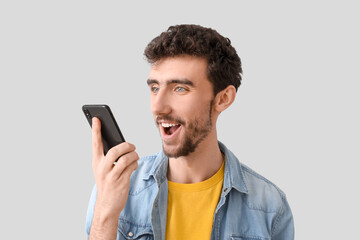 Wall Mural - Handsome young man with mobile phone sending voice message on light background, closeup