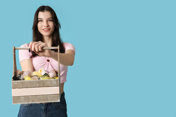 Sticker - Pretty young woman holding wooden Easter basket with cosmetics on blue background