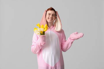 Wall Mural - Happy young man in Easter bunny costume with flowers pointing at something on white background