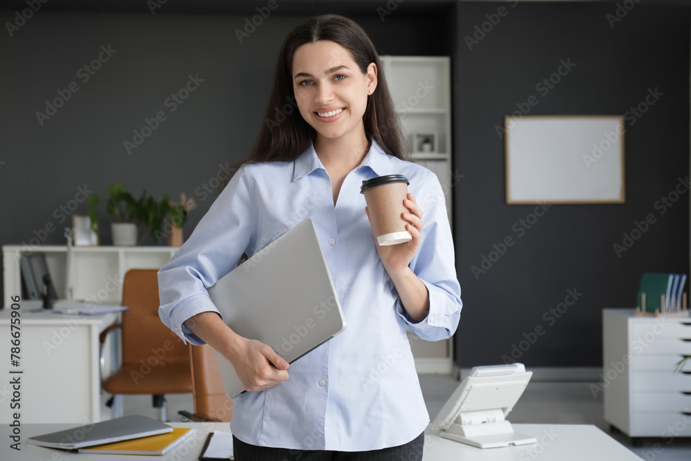 Pretty businesswoman with modern laptop drinking coffee in light office