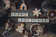 Holidays card on wooden background with gingerbread cookies, handmade craft toys, festive rustic zero waste decorations. Sustainable lifestyle. Merry Christmas greeting written with wooden blocks.