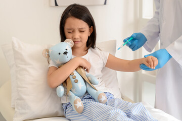 Sticker - Scared little Asian girl with toy bear receiving vaccine at hospital