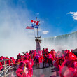 Tourists clad in red ponchos on a boat at Niagara Falls experience the mist and grandeur of the cascades, with the American and Canadian flags flying above. High quality photo. 