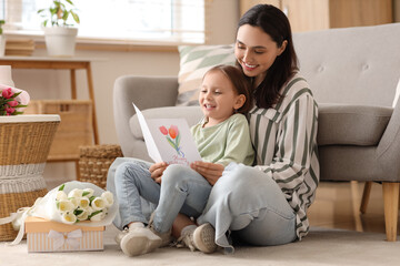 Canvas Print - Happy mother with her cute little daughter and greeting card sitting on floor at home