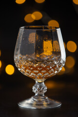 Sticker - A glass of alcohol is sitting on a table. The glass is half full and has a yellowish tint. The image has a moody and mysterious feel to it, as the focus is on the glass and the liquid inside it