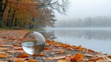 Crystal Ball With Autumn Leaves On The Shore Of Lake In Foggy Morning