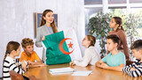 Fototapeta Londyn - Smiling young woman teacher showing state flag of Algeria and telling preteens schoolchildren history of country during lesson in class