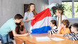 Group of preteen schoolchildren attentively watching pedagogue describing Holland flag in schoolroom