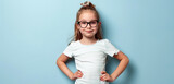 Fototapeta Motyle - In front of a light blue background, a young girl strikes a playful pose with hands on hips, her glasses adding a hint of maturity to her spirited demeanor
