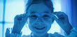 With a gentle blue hue enveloping the scene, a young girl giggles as she adjusts her glasses, her eyes sparkling with joy and innocence
