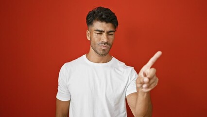 Wall Mural - Handsome young hispanic man with beard gestures no against a vibrant red wall background