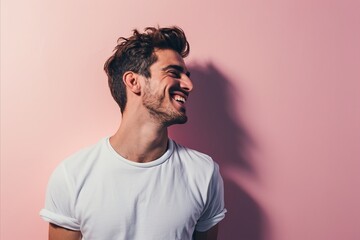 Wall Mural - Handsome young man laughing and looking away while standing against pink background