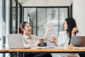 Two cheerful women having a coffee break with laptops open on their office table, engaging in a lively conversation.