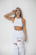 Beautiful slender blonde woman in a white top in white ripped jeans and sunglasses posing on a white background