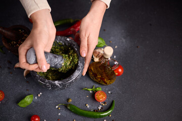 woman pounding in a stone marble mortar green sauce chopped ingredients - capers, fennel and basil