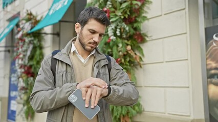 Wall Mural - Hispanic man with beard checks time on smartwatch in urban city street setting.