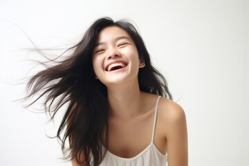 Wall Mural - A beautiful Asian woman with long straight hair  whose skin is tan is wearing an all white shirt, and smiling with a face which is full of happiness in a white room. Generative AI.