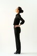 A woman in professional black clothing stands with her hand on her hip, exuding confidence and poise.