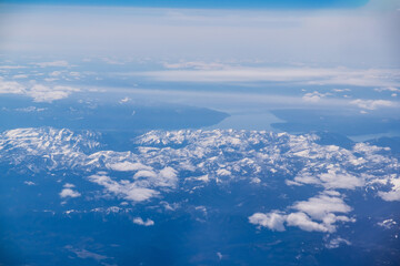 Wall Mural - an aerial view from an airplane window of mountains, snow, clouds and bright blue skies. united stat