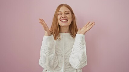 Canvas Print - Young, excited redhead woman, crazy with joy over success, triumphantly celebrates her win, standing, arms raised in victory, in a sweater against isolated pink wall.