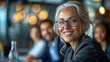 © boxstock production - Smiling senior businesswoman leader wearing glasses sitting at meeting table with group of office workers in a team in corporate conference room
