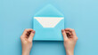 © MuhammadQaiser - First person top view photo of hands holding blue envelope and white card on isolated pastel blue background with empty space