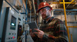 an electrician in work , wearing safety glasses and a hard hat, using a tablet to check the interconnectedness between various machines at an industrial plant