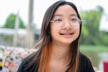 Asian girl teenage girl with eyeglasses wearing black t-shirt smiling brightly on background outdoors