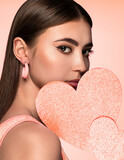 Fototapeta Tęcza - Beauty studio portrait of young beautiful woman holding peach heart against background in peach tones.