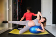 Pregnant woman doing Pilates exercise with a ball workout at a gym with a personal trainer.