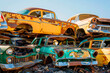 Old rusty yellow and green cars piled up in a scrapyard.