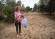 Caucasian Woman Picking Up Trash in a Forest, Participating in Environmental Cleanup