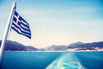 Wall Mural - national flag of greece on a ferry on the background of greek island landscapes and the trace of the