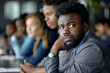 © AI_images - An Afro-American businessman attentively listens to a discussion amidst a corporate meeting.
