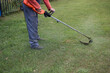 © Александр Лебедько - A man mows the grass in front of his house with a trimmer. A man uses an electric trimmer to cut grass on his lawn. Maintaining the area in front of the house and mowing the grass using a trimmer.