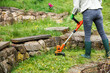 Woman is trimming grass next stone wall in garden. Lawn care by grass trimmer