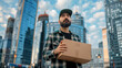 A delivery man wearing a green cap and plaid shirt is holding a cardboard box while looking up at a tall building.