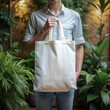 Tote bag mockup. Man holding reusable white cotton linen eco organic fabric canvas blank totebag with green leaves plant trees background. AI generated
