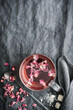 Eine Tasse Tee mit pinken Rosenblättern auf einem grauen Leinen Tischtuch. Draufsicht, Heißgetränk.