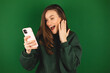 Overjoyed happy excited woman say wow, glad to receive text message informing about salary, rejoices good news, stares at mobile phone, gestures actively from happiness isolated green background.